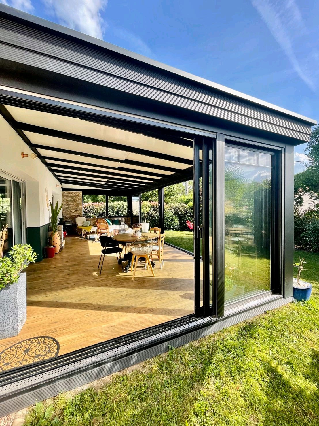 Véranda moderne en aluminium attenante à une maison, baignée de lumière naturelle avec vue sur le jardin